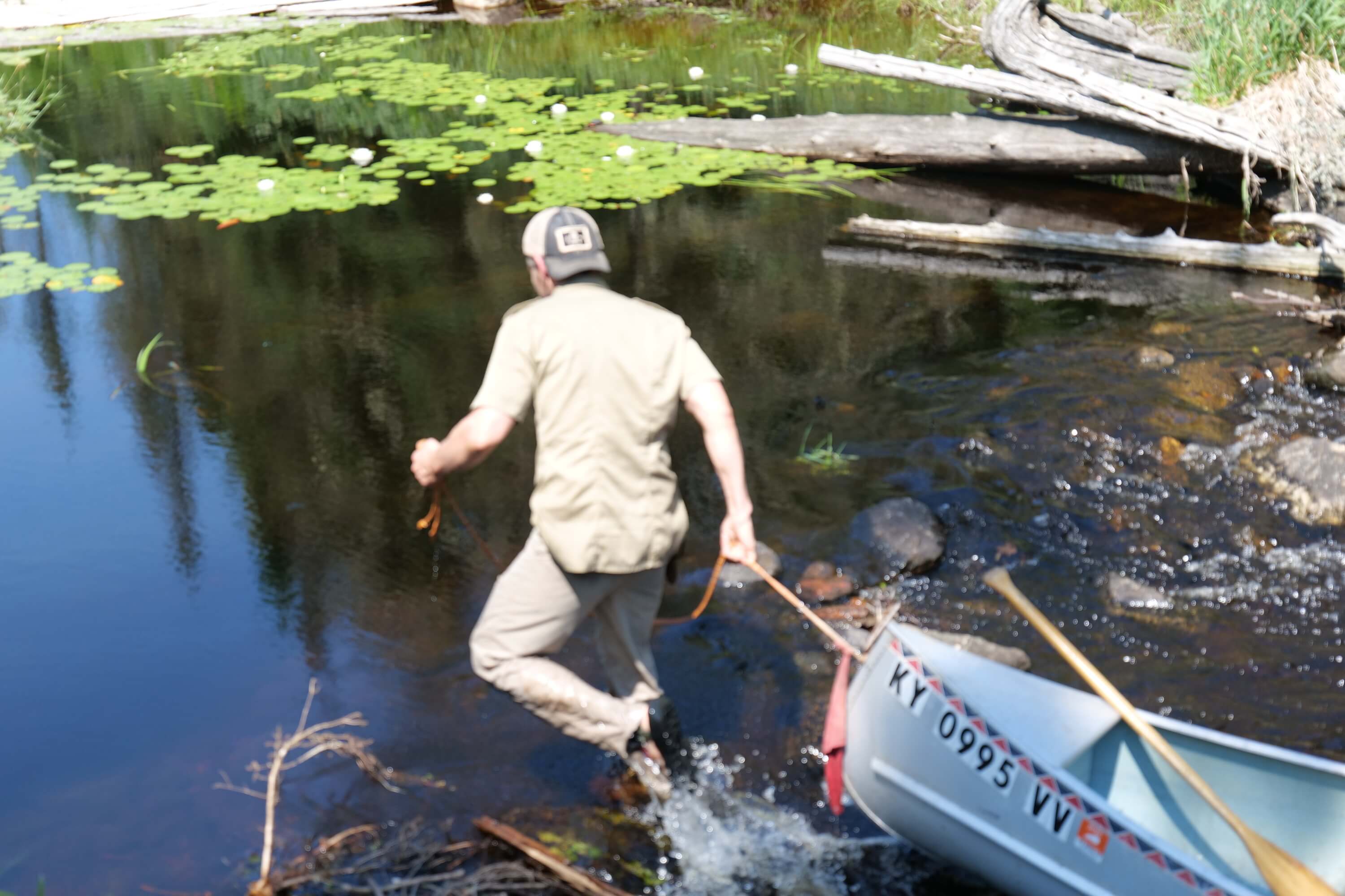 Man lining a canoe through shallow rocky water on a backcountry river